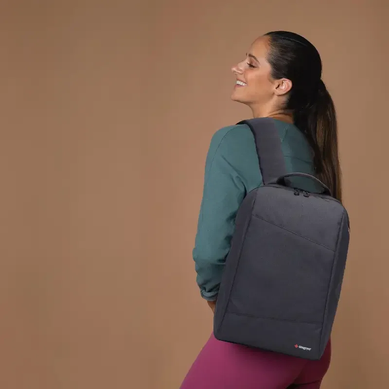 Mujer sonriente con mochila negra sobre un fondo marrón.